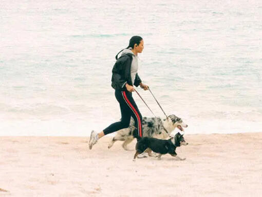 A woman runs along the beach with two dogs